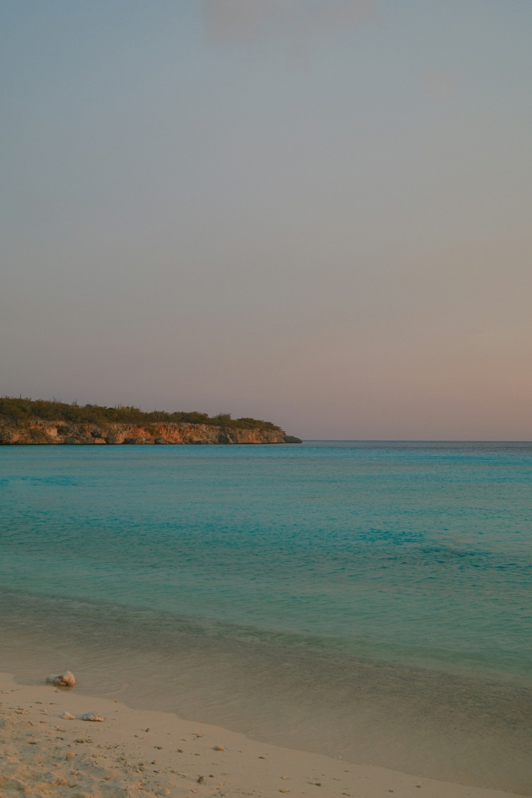 A quiet Curaçao beach at dusk with pastel skies over calm water