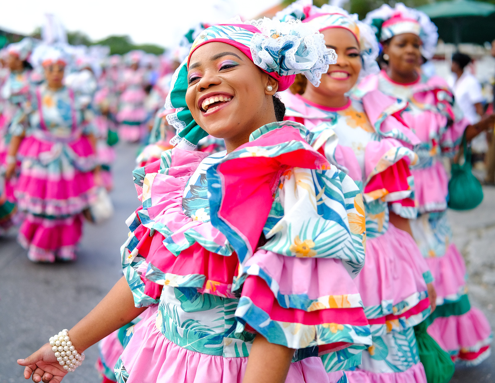 Dancers in vibrant pink floral folklore costumes during the Seú harvest parade in Curaçao