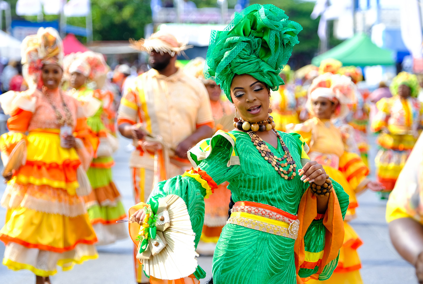 A Seú dancer in a bright green traditional dress and headwrap with layered beaded necklaces