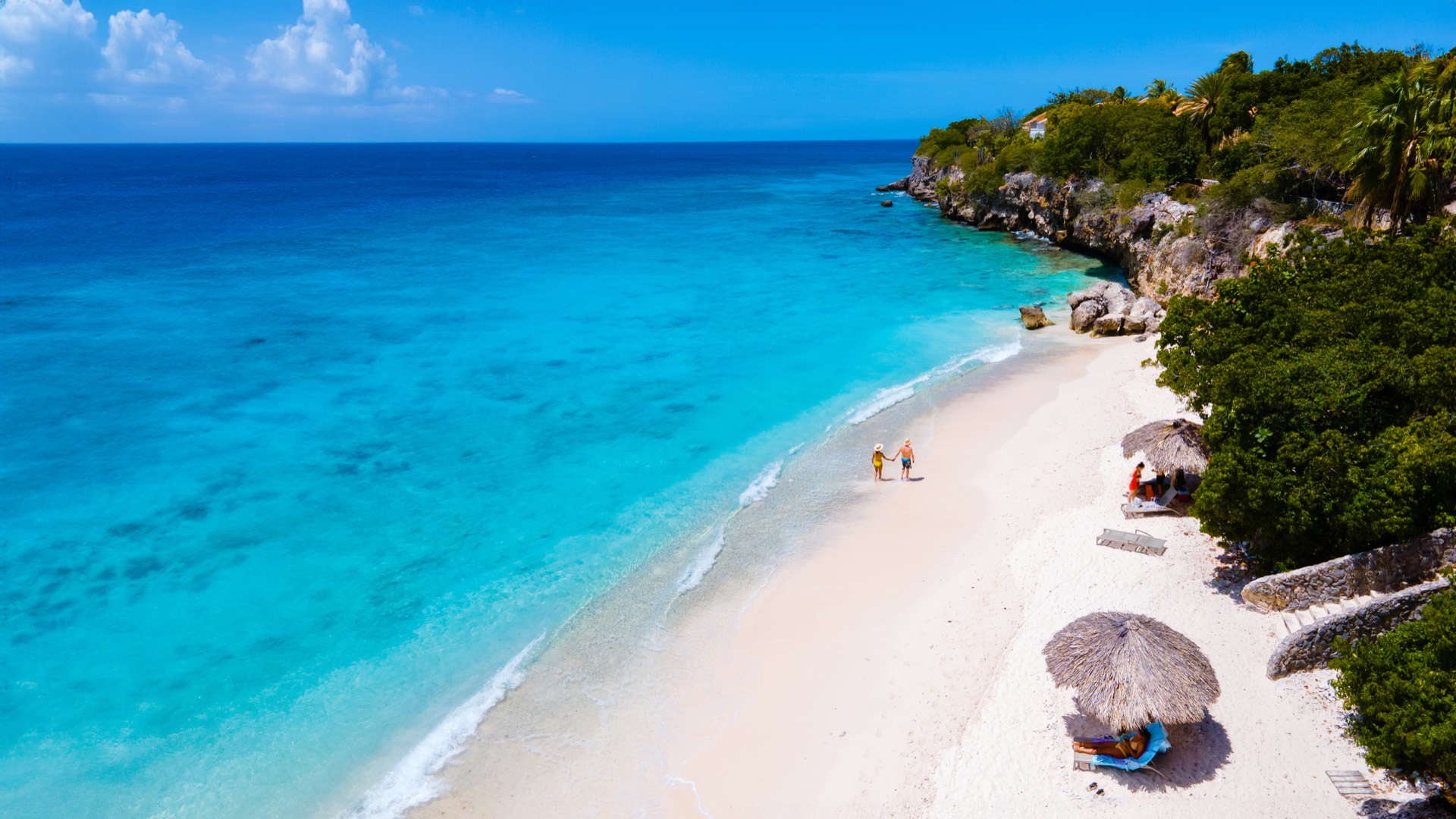 Aerial view of a turquoise Curaçao beach with white sand and palapas